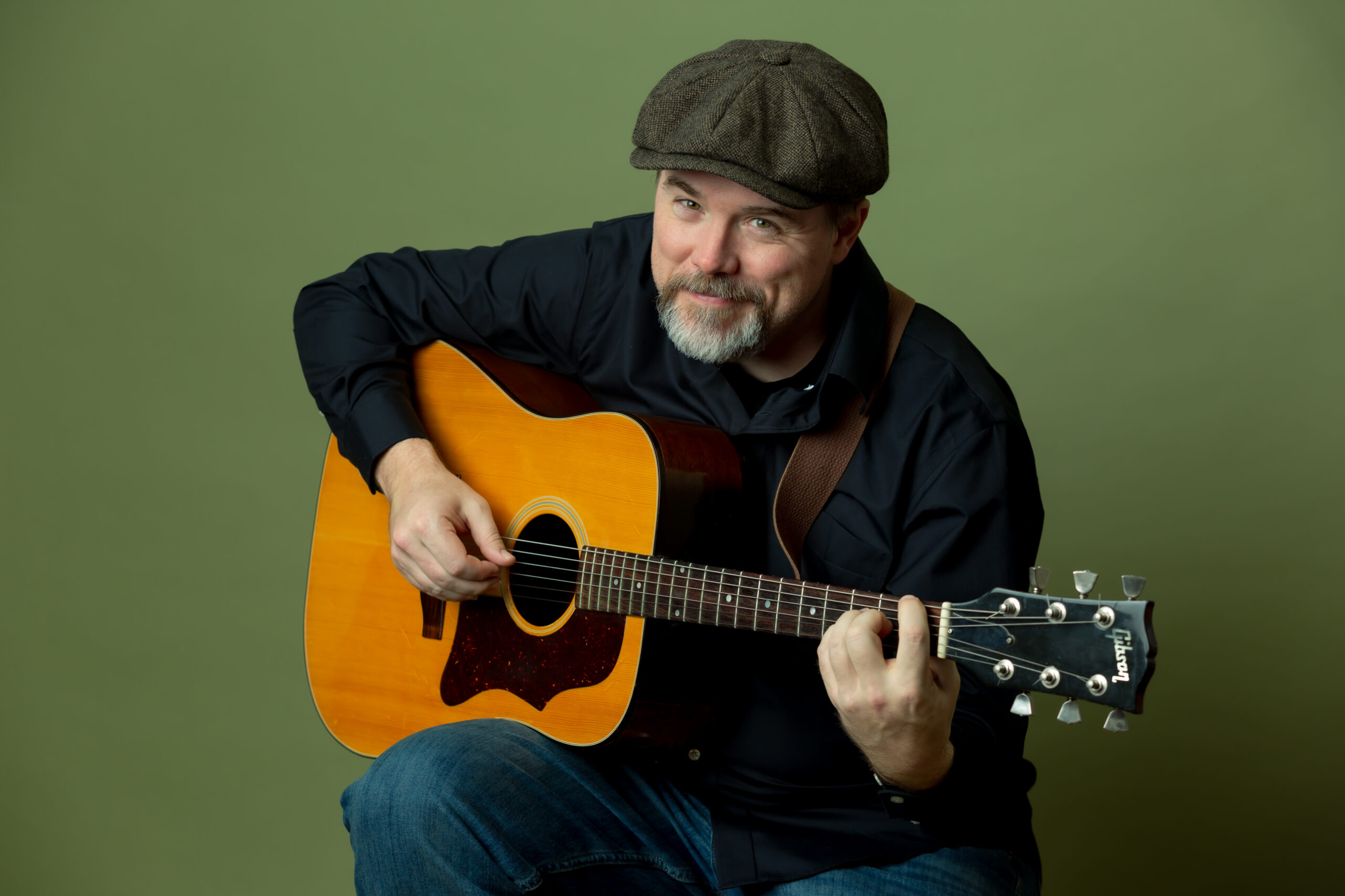 Photo of Paul Strickland playing a guitar in front of a green background